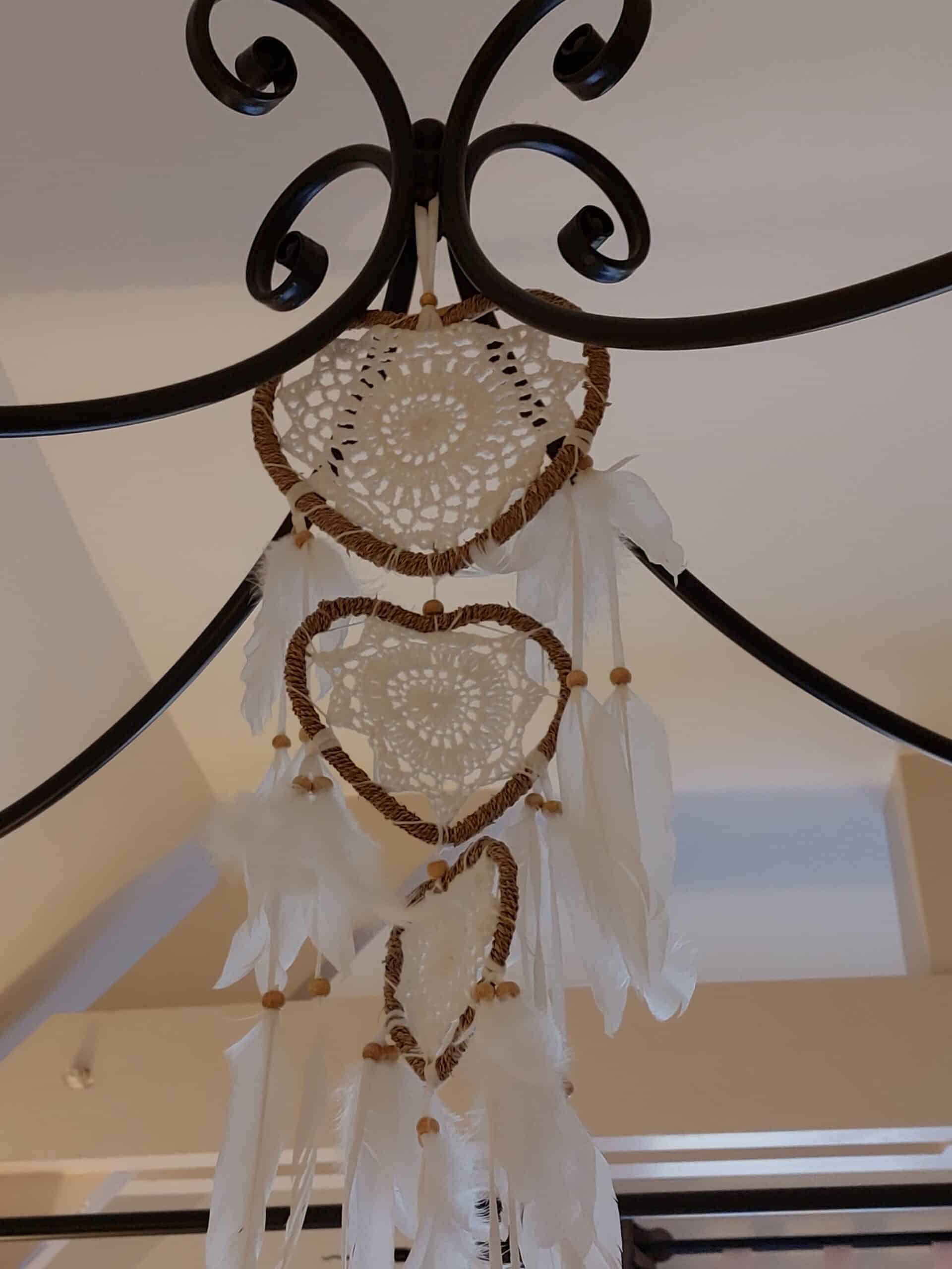 Attrape-rêves romantique triple cœur suspendu. Crochet blanc, corde marron, plumes et perles. Cadre de lit en métal noir.
