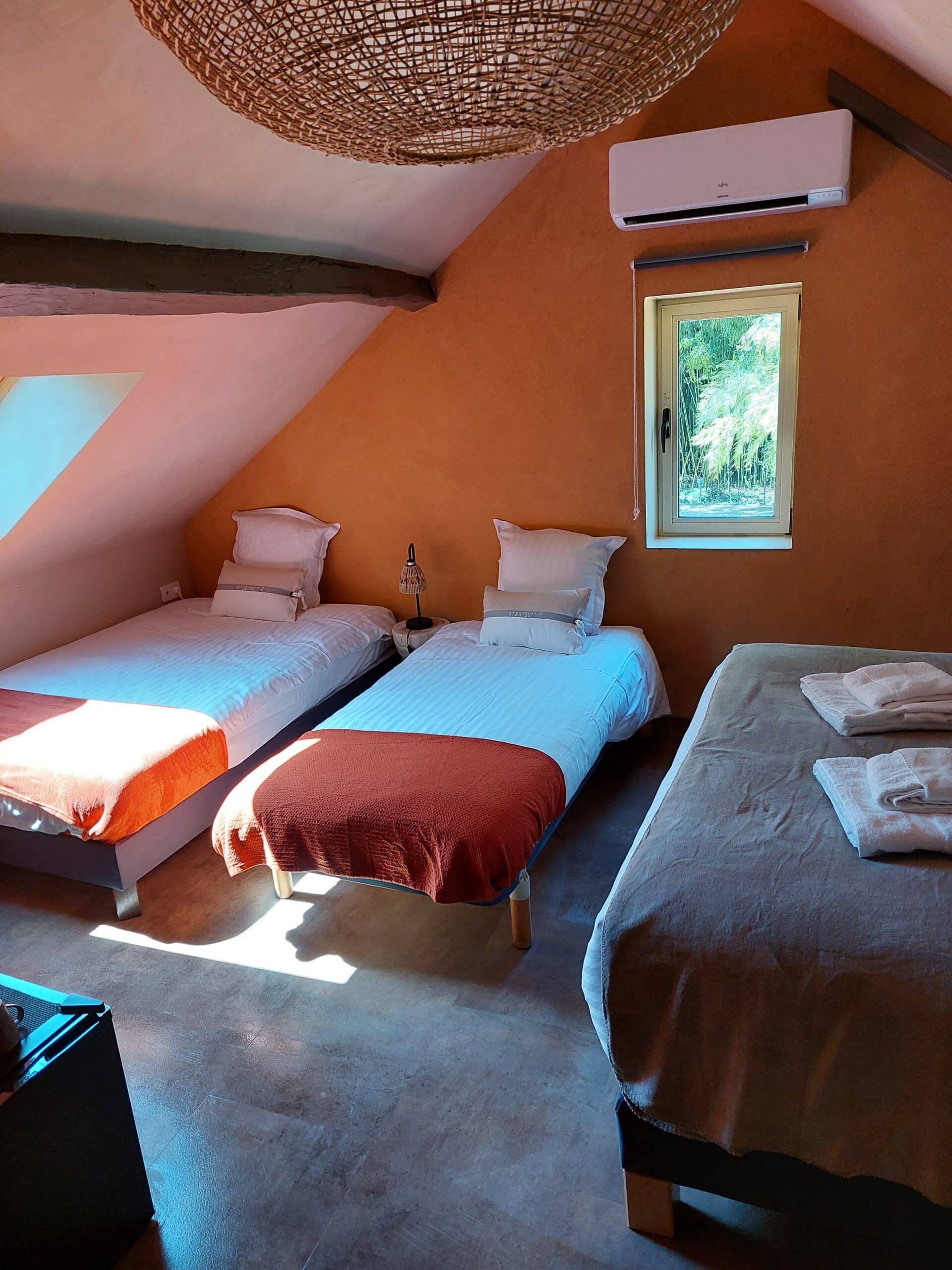 Chambre de gîte mansardée aux murs terre cuite. 3 lits simples. Lumière naturelle éclatante. Climatisation Fujitsu.