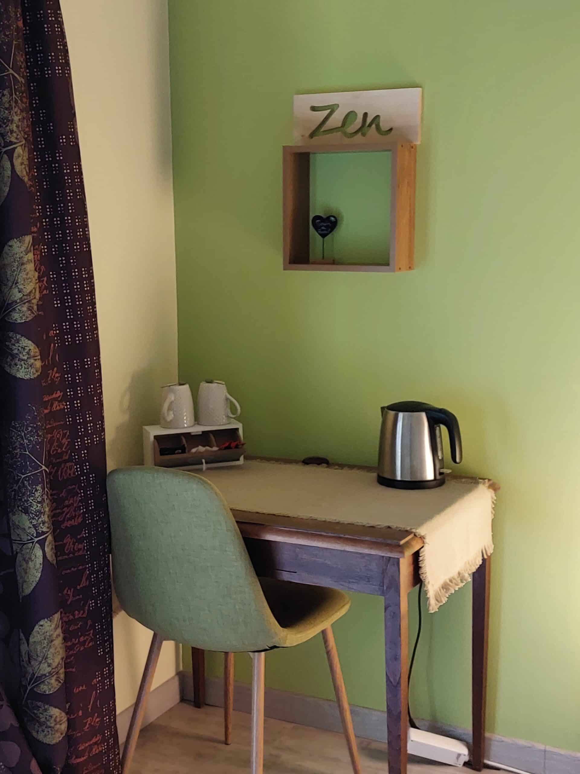 Coin thé dans un intérieur moderne : mur vert, panneau "Zen" sculpté, bouilloire inox sur table en bois et chaise vert olive.