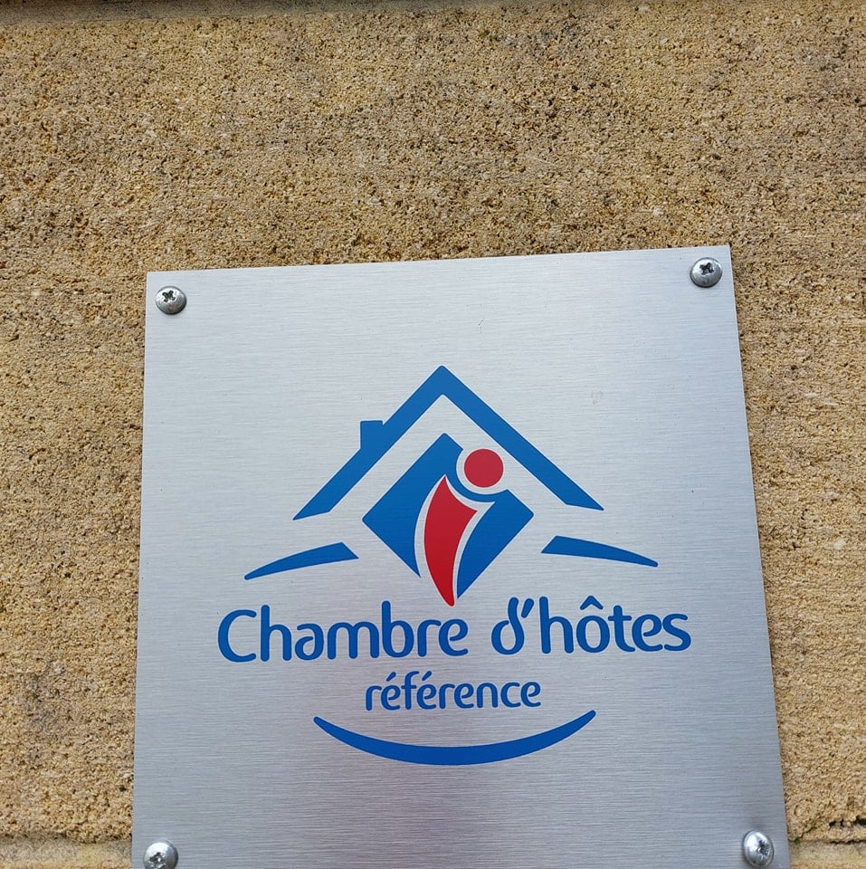 Chambre d'hôtes Référence | Plaque officielle qualité. Plaque métallique brossée fixée au mur. Logo Chambre d'hôtes référence en bleu et rouge, indiquant une qualité d'hébergement.