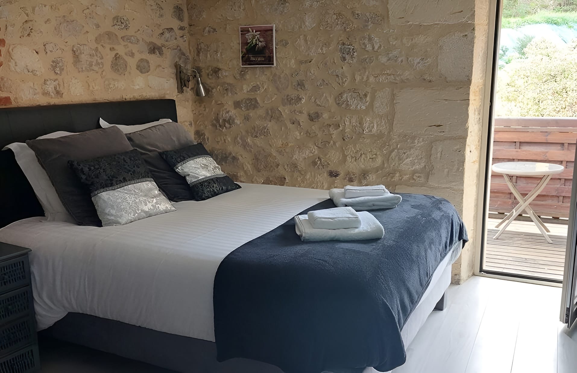 Pont en pierre, terrasse de restaurant provençale Petit pont de pierre sèche et moellons au-dessus d'un canal d'eau, menant à une terrasse de restaurant avec tables sous une structure en bois à toiture de tuiles.